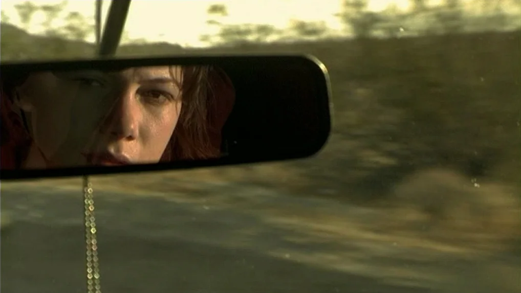 Land of Plenty (2004) movie still: closeup — A view inside a car through the rearview mirror showing a woman's face. The desert landscape passes by…