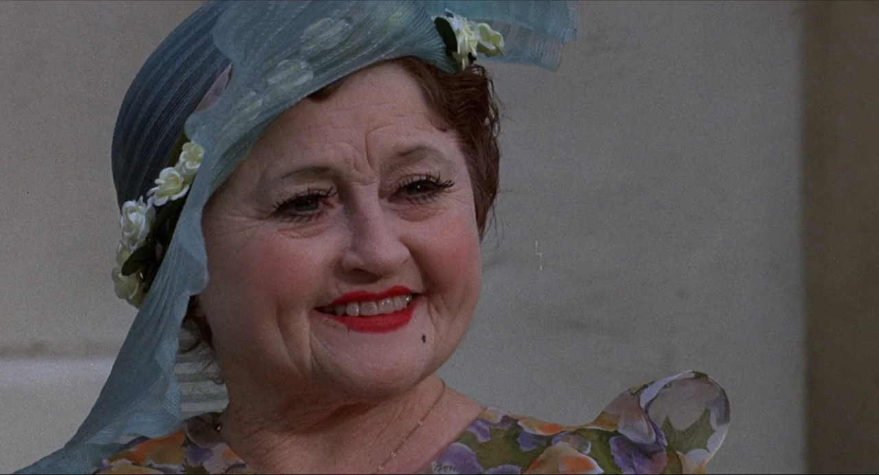 What’s the Matter with Helen? (1971) movie still: closeup — An older woman stands outdoors against a plain, light-colored background. She wears an…