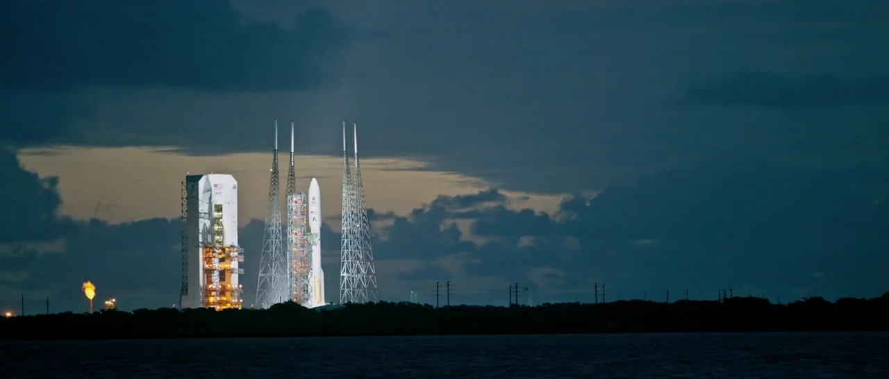 The Martian (2015) movie still: wide — A tall space launch vehicle sits on a coastal pad under a dark twilight sky. The rocket is flanked by tall…