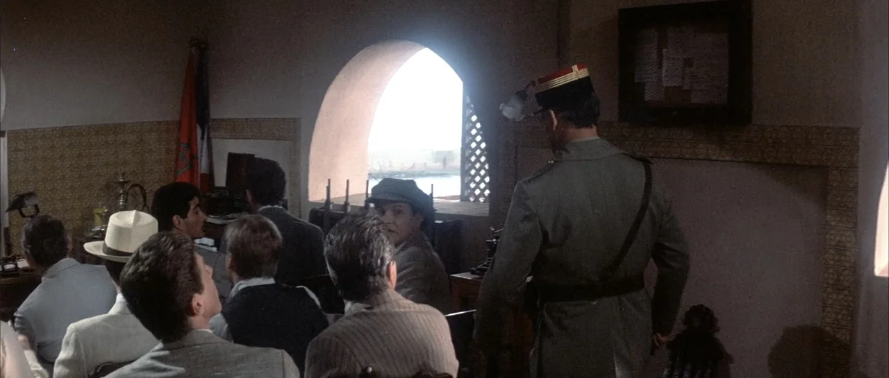 Sahara (1995) movie still: medium — A dimly lit administrative room features an arched window and patterned tile wall sections. A uniformed soldier…