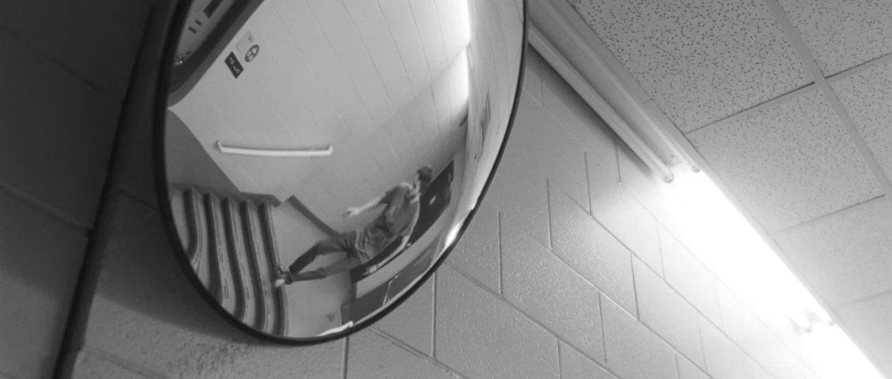 Polytechnique (2009) movie still: medium — A institutional corridor features a convex security mirror mounted on a painted cinder block wall. The…