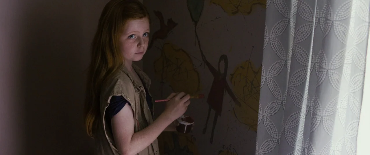 Sinister (2012) movie still: medium — A dimly lit room features a child painting on a light-colored wall mural. The subject looks toward the viewer…