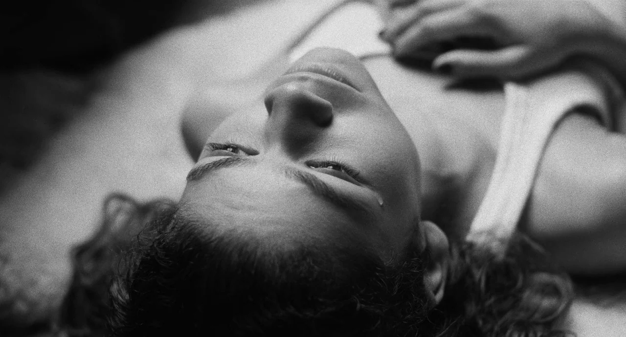 Malcolm & Marie (2021) movie still: A raw, intimate, black-and-white close-up of a young woman lying on her back, lost in deep, mournful thought.…