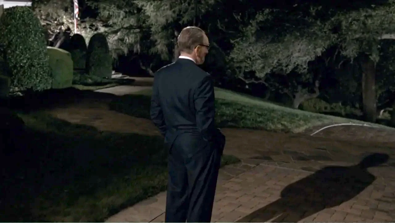 All the Way (2016) movie still: fullbody — A paved backyard patio area is surrounded by dark trees and dense garden foliage. An older man in a…