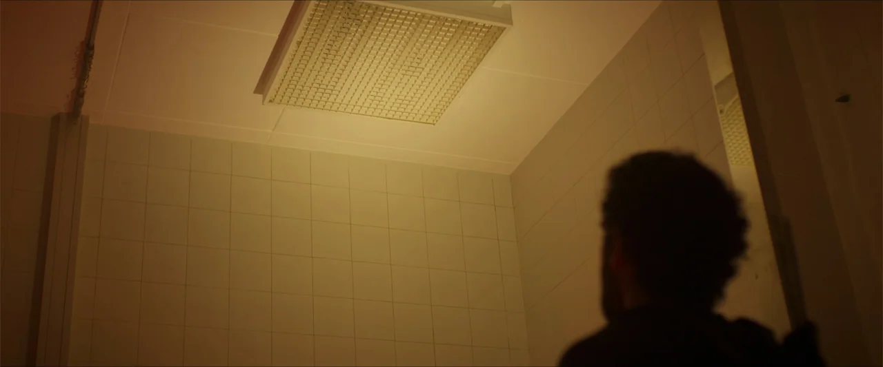 Apocalypse Z: The Beginning of the End (2024) movie still: medium — A sterile public restroom features tiled walls and a recessed ceiling lighting…