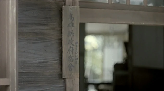 A Time To Love and A Time To Die (1985) movie still: closeup — An aged, dark wooden exterior wall holds a vertical name plate featuring Japanese…