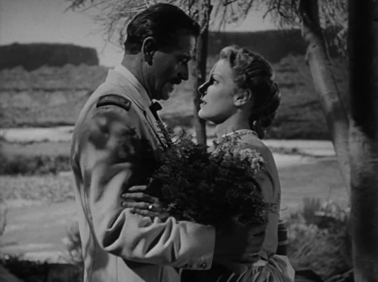 Rio Grande (1950) movie still: medium — An open field with sparse trees and distant mesas provides the setting. A military officer and a woman stand…
