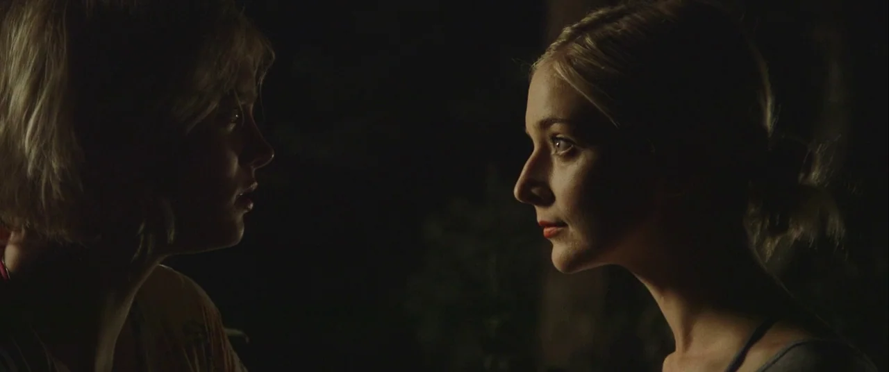 Always Shine (2016) movie still: medium — Two young women face each other in an outdoor nighttime environment. The scene is pitch black beyond the…