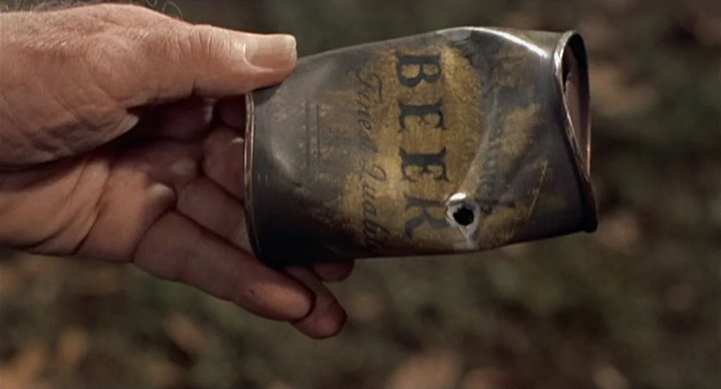 The Trouble With Harry (1955) movie still: closeup — A close-up of a human hand holding a dented, weathered vintage metal beer can. The can has a…