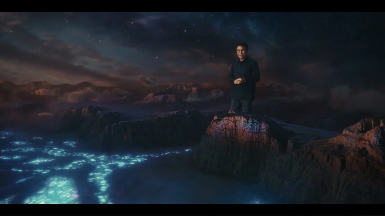 Lee Soo Man: King of K-Pop (2025) movie still: wide — A man stands atop a craggy rock formation surrounded by a vast cosmic landscape. The ground…