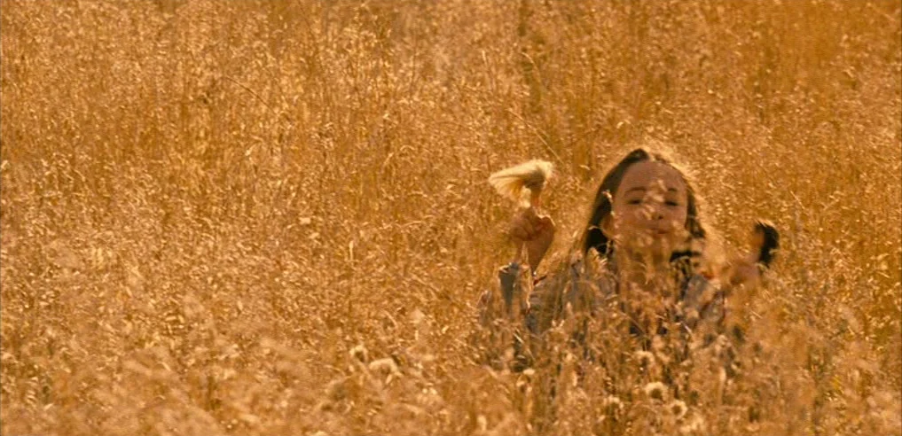 Tideland (2005) movie still: medium — A field of tall, dry, golden grass fills the frame under warm light. A young girl is visible from the chest…