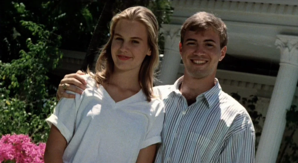 Rhapsody in August (1991) movie still: medium — A man and woman pose outdoors in front of a white classical architectural structure. The man puts…