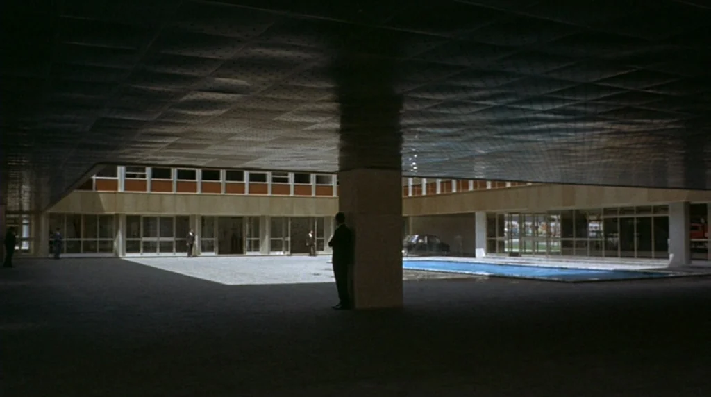 Danger Diabolik (1968) movie still: wide — A modern architectural courtyard features a central pool and long, glass-fronted multi-story buildings.…