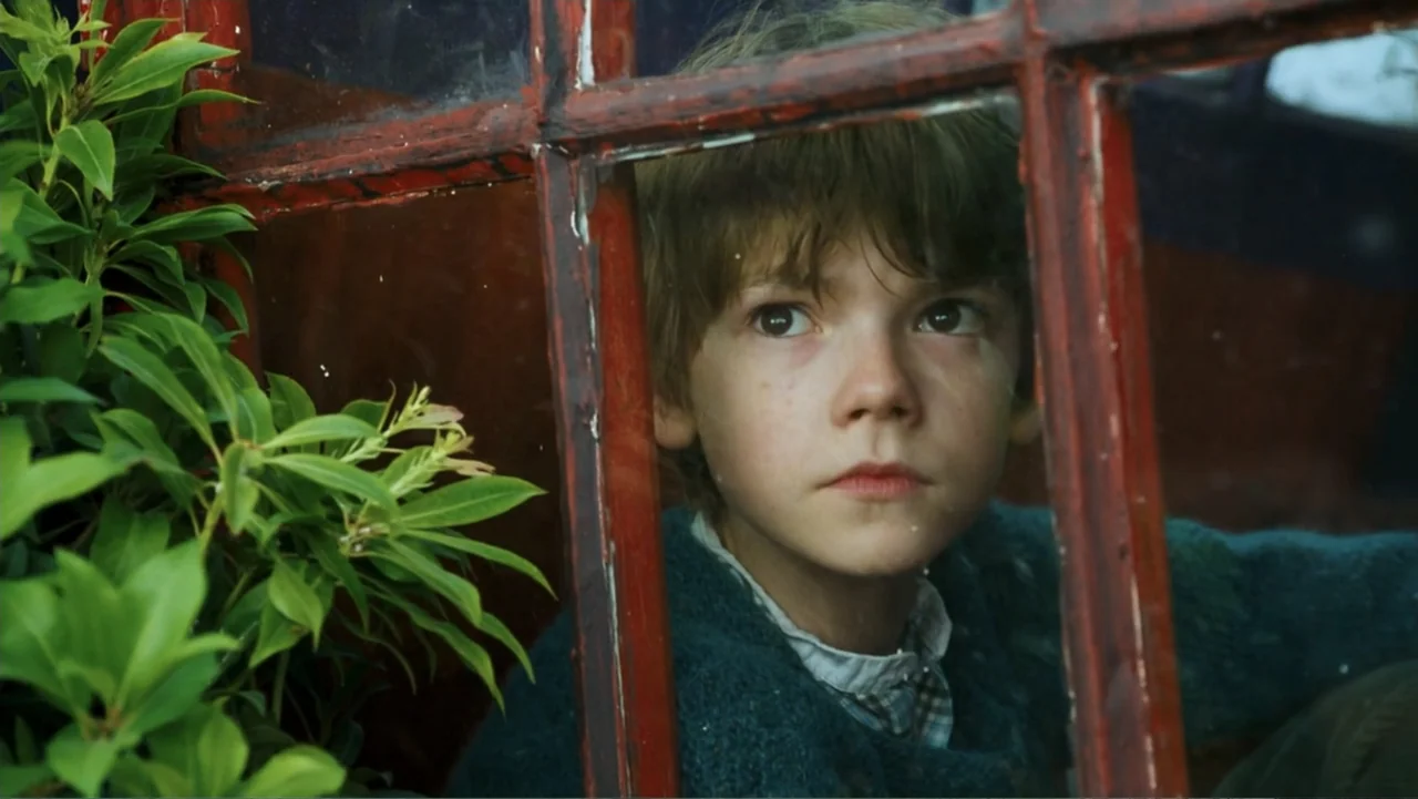 Nanny McPhee and the Big Bang (2010) movie still: closeup — A young boy sits behind a red-painted wood window frame with glass panes. He gazes…