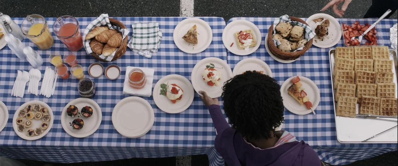 Final Destination 5 (2011) movie still: wide — A long table covered with a blue and white checkered cloth displays many breakfast foods. A person…