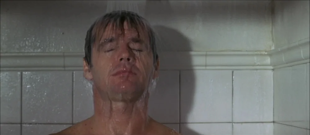 Carnal Knowledge (1971) movie still: closeup — A tiled stall features white, square ceramic wall tiles with a molded border. A man stands with his…