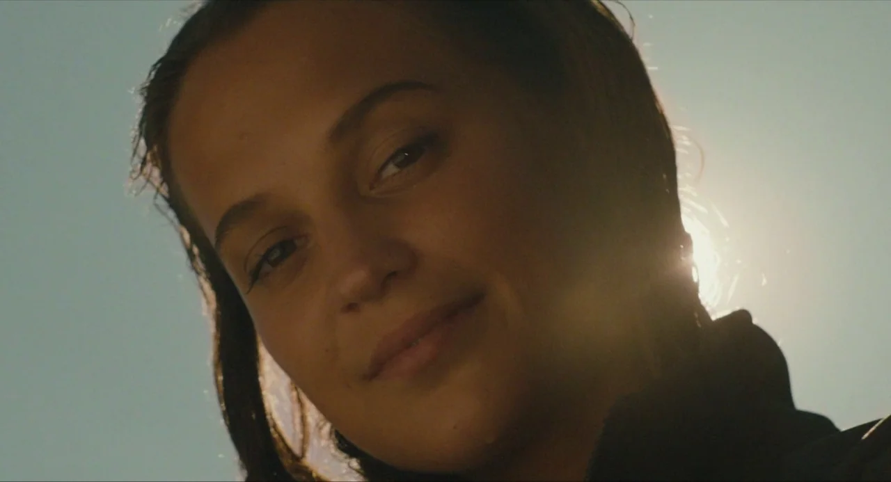 Submergence movie still: closeup — A person is positioned against a bright, clear sky over open water. A woman with wet hair looks downward toward…