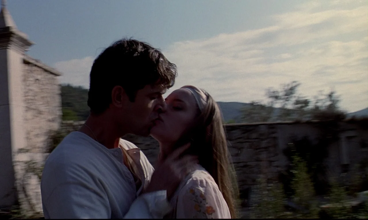 Dellamorte Dellamore (1994) movie still: medium — An outdoor courtyard with stone walls stands under a bright sky. A man and woman embrace each…
