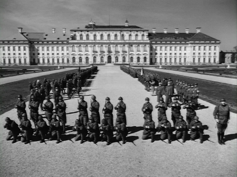 Paths of Glory (1957) movie still: wide — A grand, symmetrical white stone palace looms over a wide, paved courtyard area. Many soldiers in uniform…