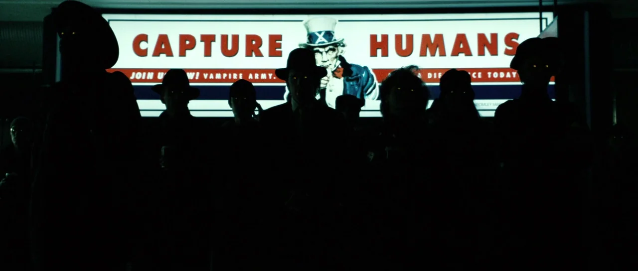 Daybreakers (2009) movie still: medium — A dark, dimly lit indoor public transport area displays a large backlit propaganda sign. Several shadowy…