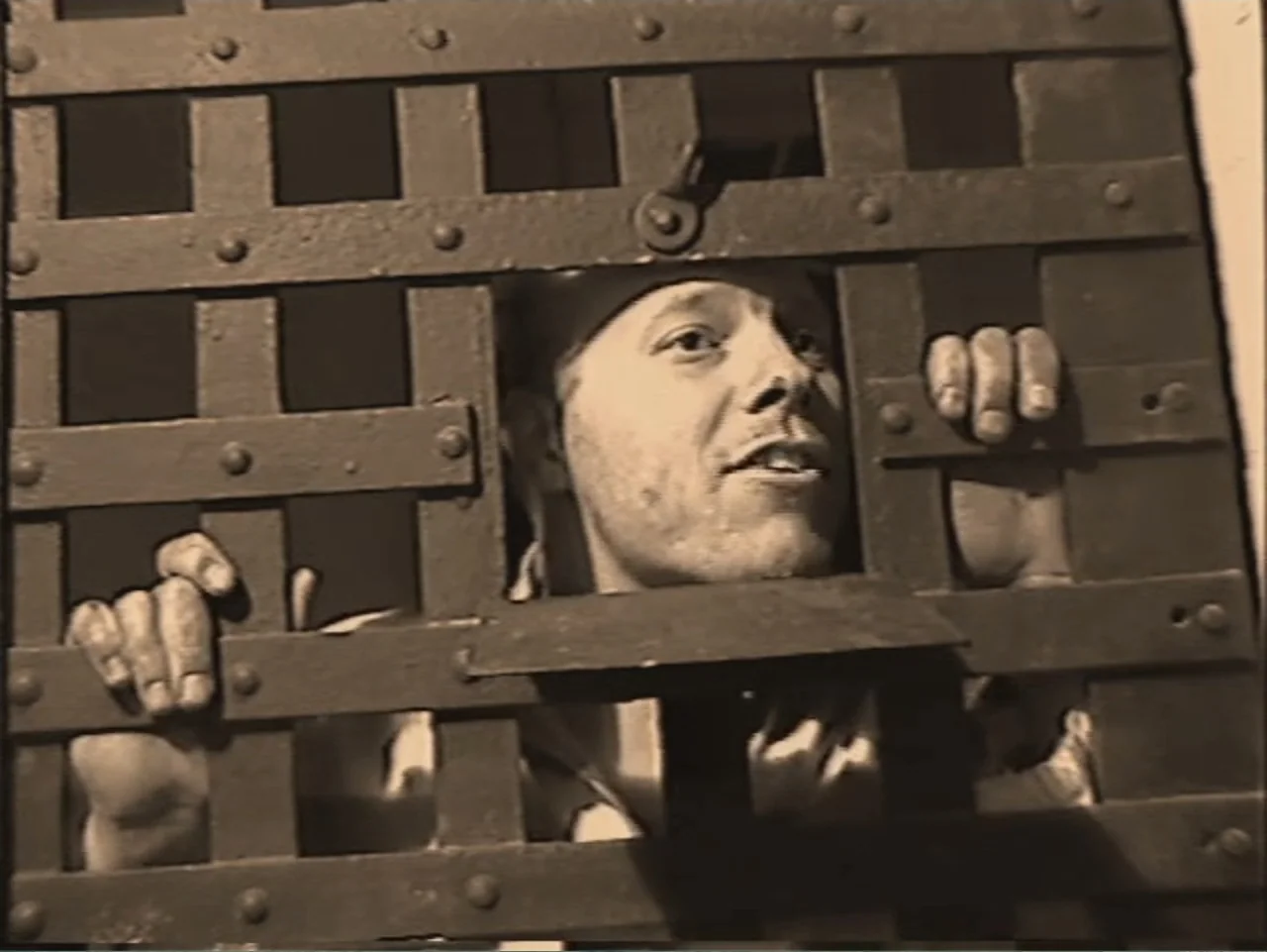 Dracula, Prisoner of Frankenstein (1972) movie still: closeup — A dark jail cell interior features heavy horizontal and vertical iron bars. A man…