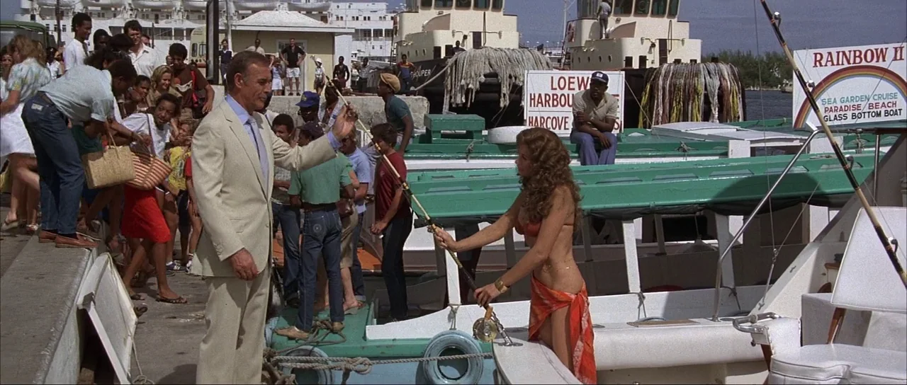 Never Say Never Again (1983) movie still: fullbody — A bustling harbor dock area features several white and green glass-bottom tour boats moored. A…