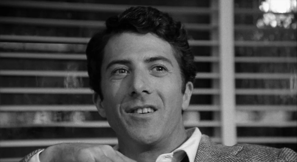 Lenny (1974) movie still: closeup — A man sits in front of white horizontal blinds inside a home. He looks off-camera with a subtle, pleasant…
