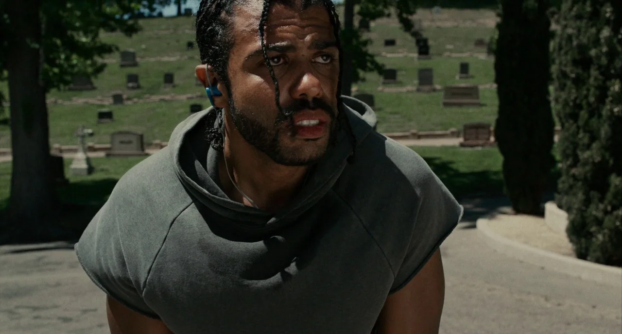 Blindspotting (2018) movie still: medium — A sunny cemetery features rows of gravestones dotting a green hillside. A man in a grey hoodie stands in…
