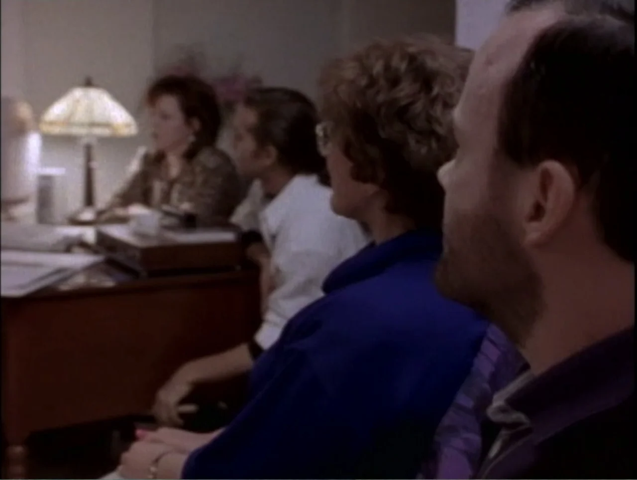 America Undercover: Life Afterlife (2000) movie still: medium — A dimly lit professional space features a group of people sitting at a desk. The…