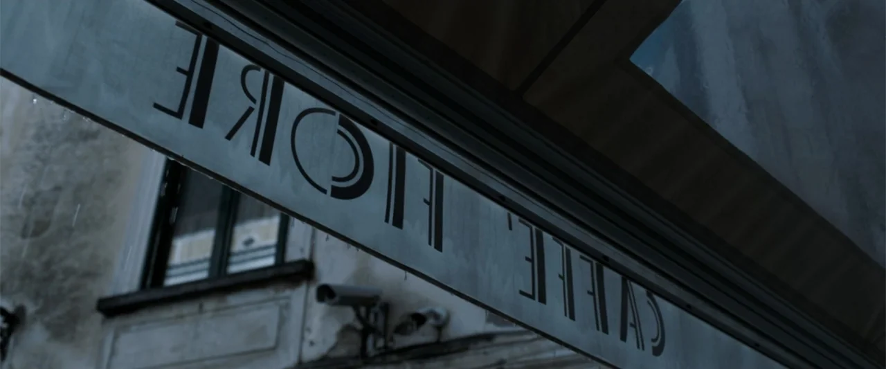 The Equalizer 3 (2023) movie still: wide — An exterior view looking up at a cafe awning with visible signage in rain. The facade is worn and…
