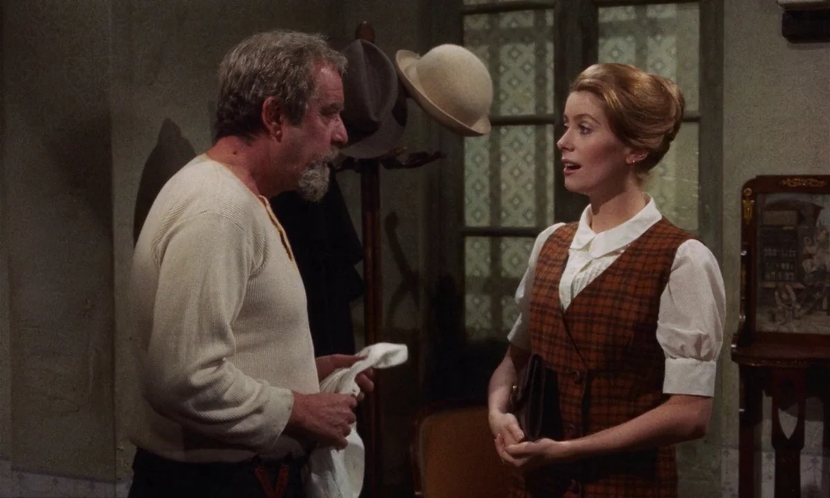 Tristana (1970) movie still: medium — A furnished apartment with a coat rack and small glass panel door in background. A man faces a young woman…
