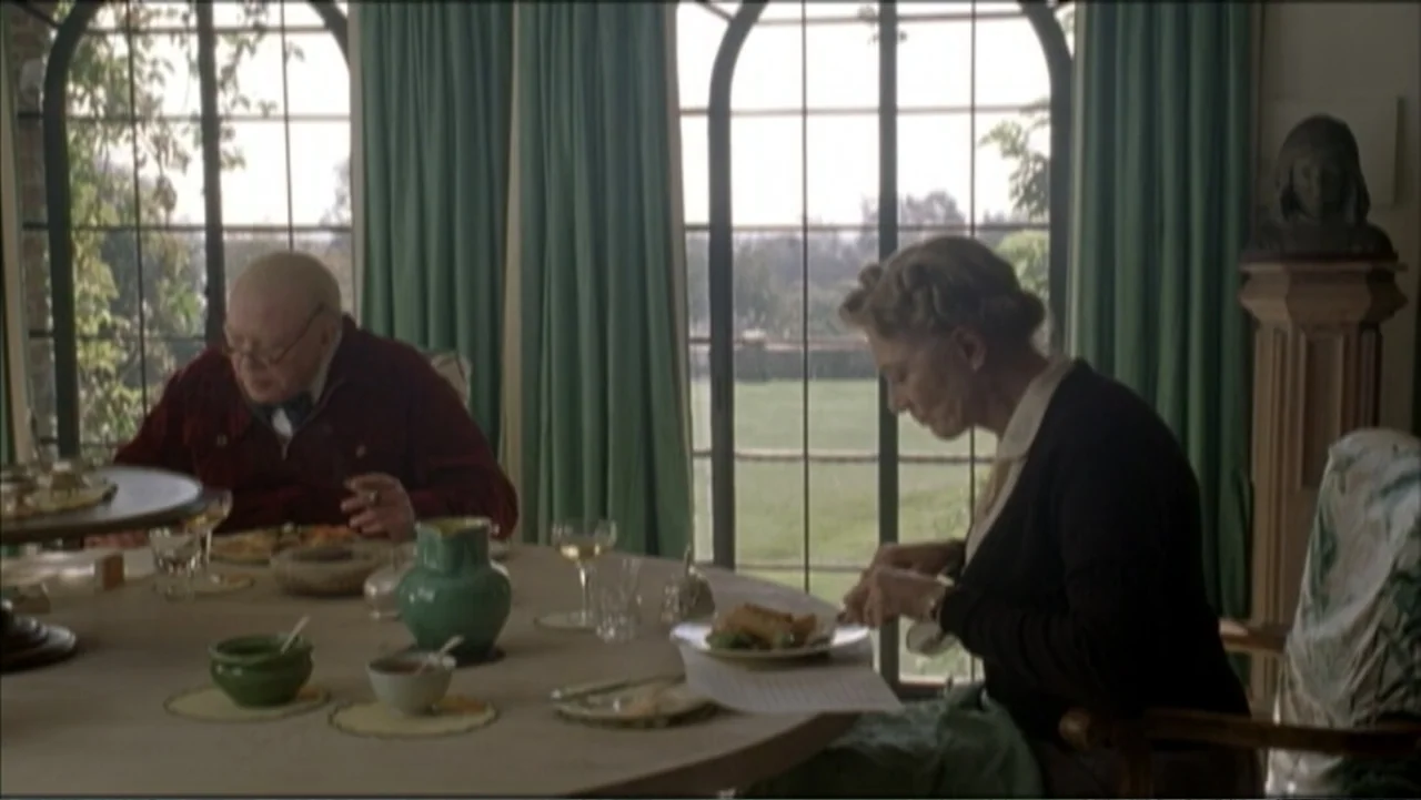 The Gathering Storm (2002) movie still: medium — A dining room features large arched windows with green curtains and a round table. An older man and…