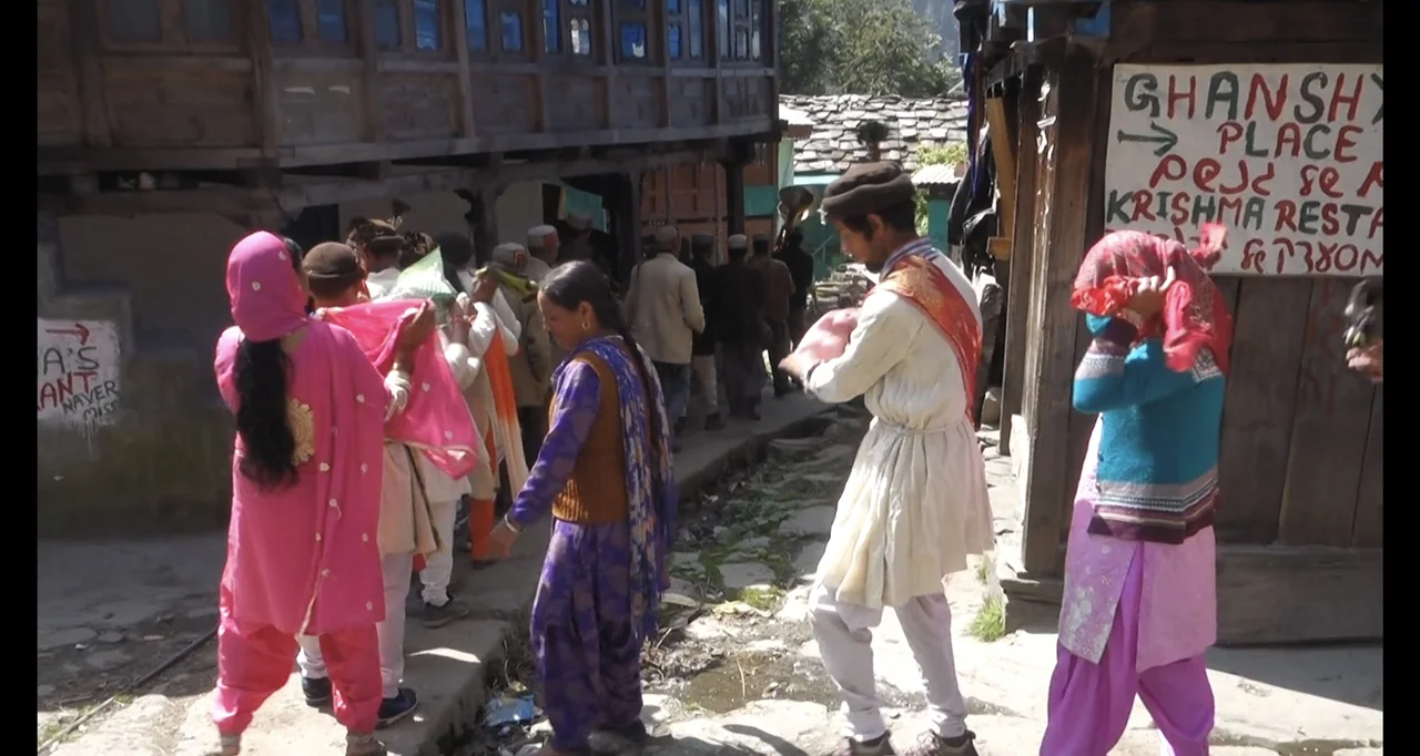 Blutch (2018) movie still: fullbody — A narrow dirt path winds between rustic multi-story wooden buildings in a village. A procession of people in…