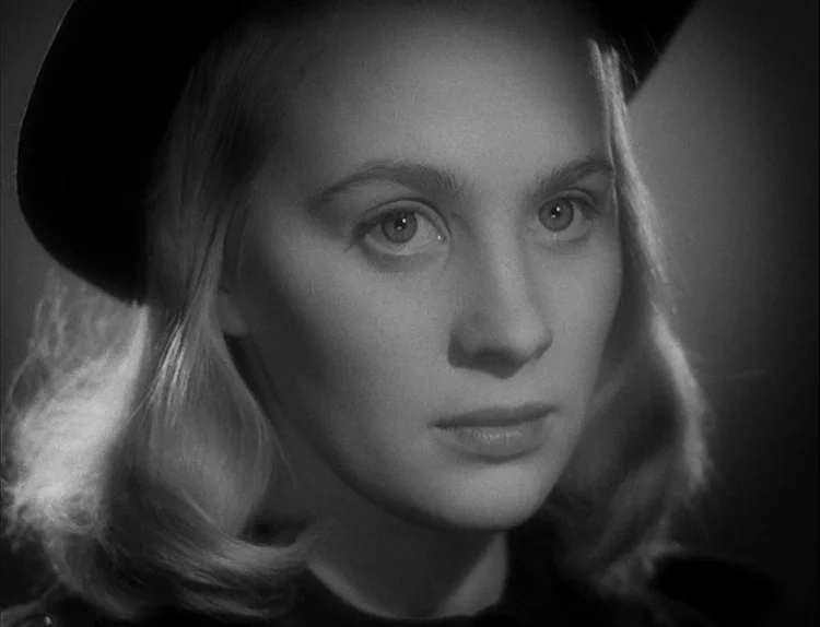 Music in Darkness (1948) movie still: closeup — A dark, undefined interior space serves as the background for a portrait. A blonde woman in a hat…