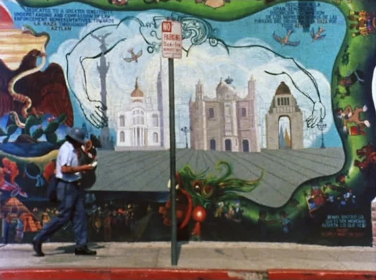 Mur Murs (1981) movie still: fullbody — A man walks past a large, colorful painted mural featuring architecture on a concrete sidewalk. The mural…