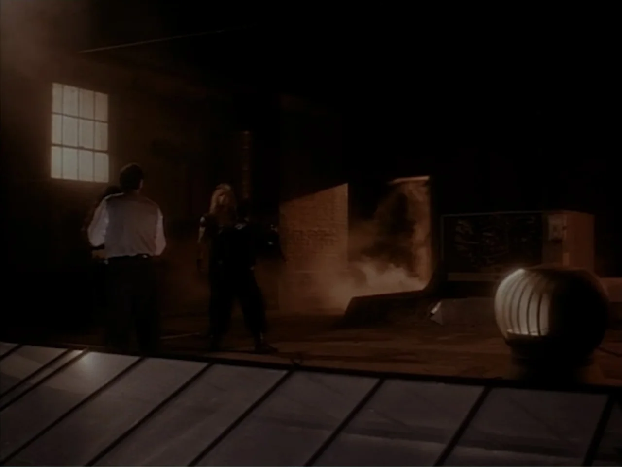 Firepower (1979) movie still: wide — A dark industrial space features thick atmosphere with a single bright window opening.