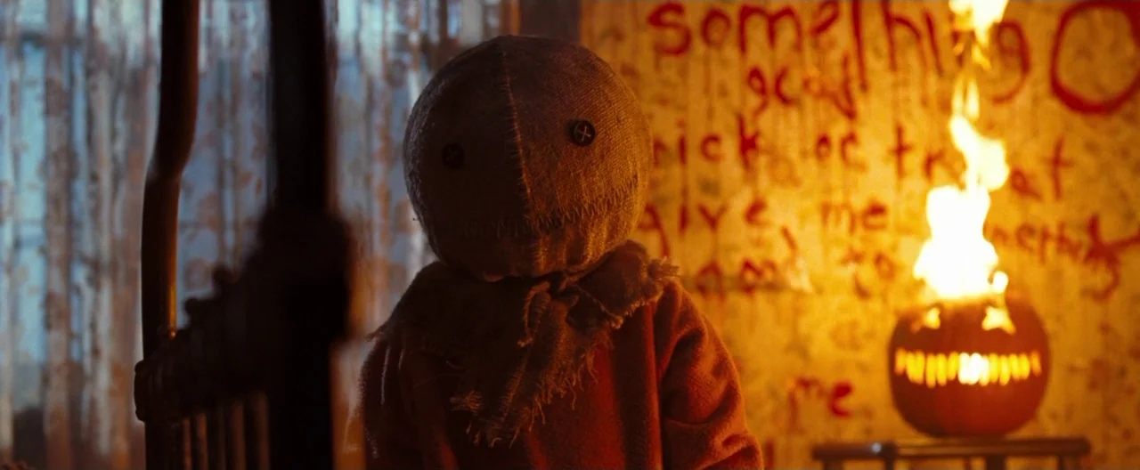 Trick ‘R Treat (2007) movie still: medium — A dimly lit indoor space features a wall covered in hand-written red text. A costumed figure stands in…