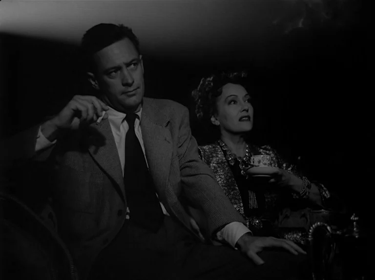 Sunset Boulevard (1950) movie still: medium — A darkened interior room with low-key lighting highlighting two individuals watching a film…