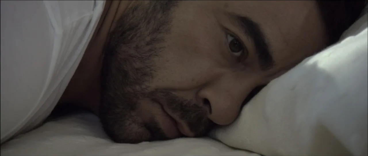 Otro verano (2013) movie still: closeup — A close-up view of a person resting on a white pillow in a dark room. The subject, a man with a beard,…