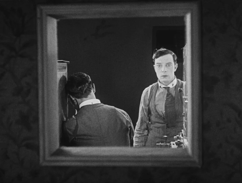 Sherlock Jr. (1924) movie still: medium — A man in formal attire stands in front of a rectangular wall mirror. His reflection is visible while he…
