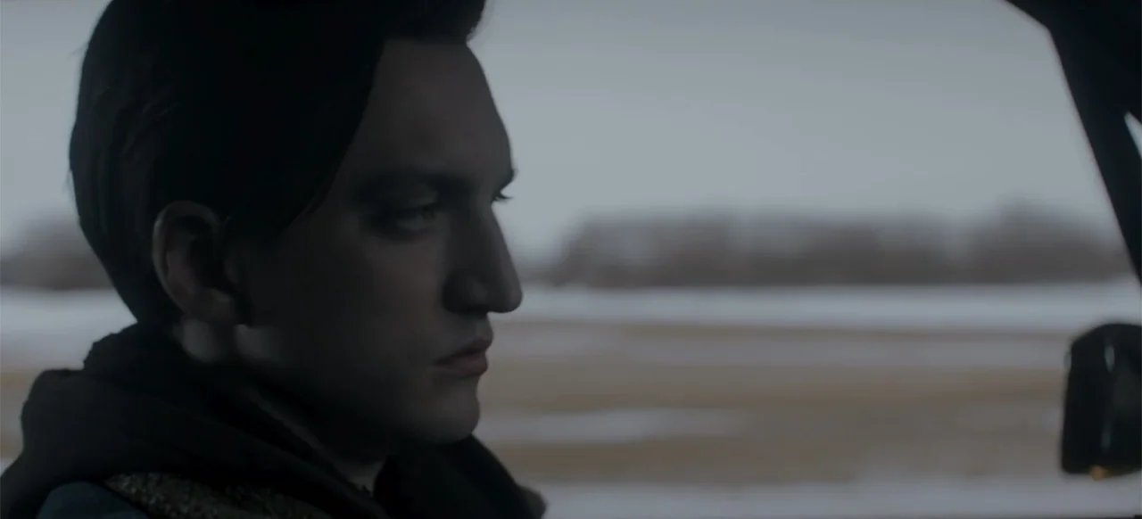 I Still See You (2018) movie still: closeup — Inside a vehicle looking out across a flat, snow-covered landscape under an overcast sky. A young man…