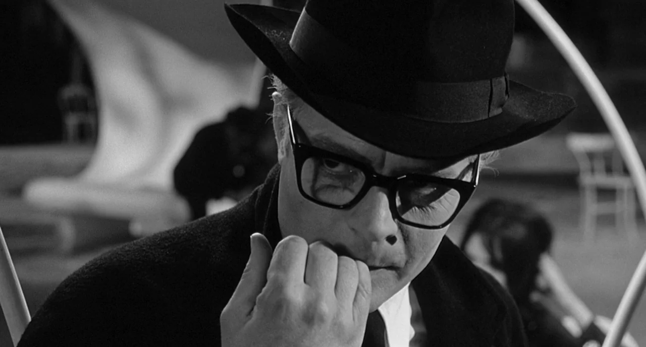 8 1/2 (1963) movie still: closeup — A dark outdoor setting features a man in a hat at night. He stares intensely while biting his own fingernails.