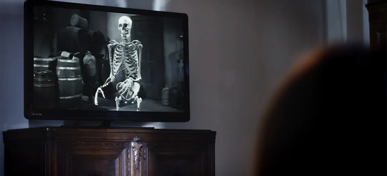 The Russian Bride (2019) movie still: medium — A dimly lit room features a television set displaying a classic black-and-white film. The viewer sits…