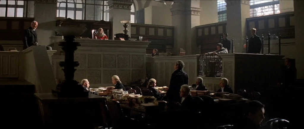 The Prestige (2006) movie still: wide — A spacious period courtroom features wood paneling, high windows, and rows of desks. Multiple figures in…