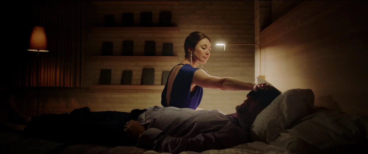 The Feast (2021) movie still: medium — A modern, dimly lit room features brick walls decorated with small framed rectangular objects. A woman in a…