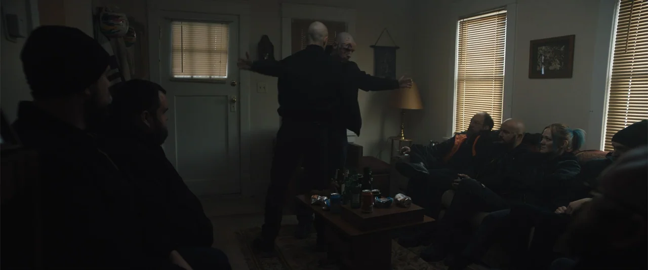 Skin (2009) movie still: medium — A dimly lit room with closed blinds and a coffee table covered in discarded cans. A man stands in the center…
