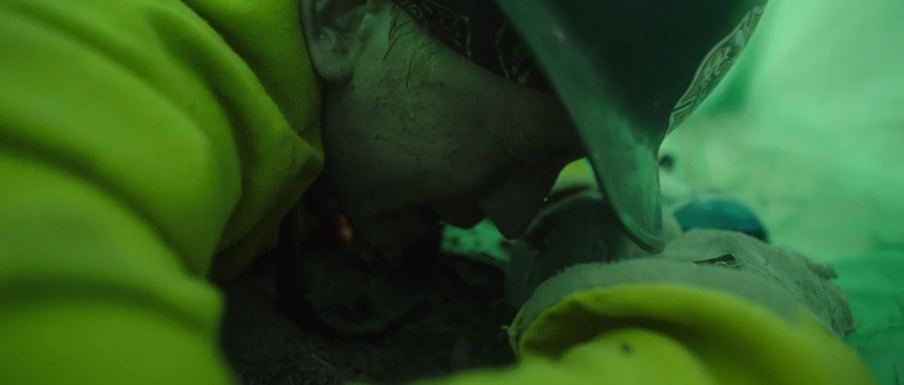 Only The Brave (2017) movie still: closeup — A person wears a hard hat while positioned on dirt inside a green tent. The man presses his forehead…
