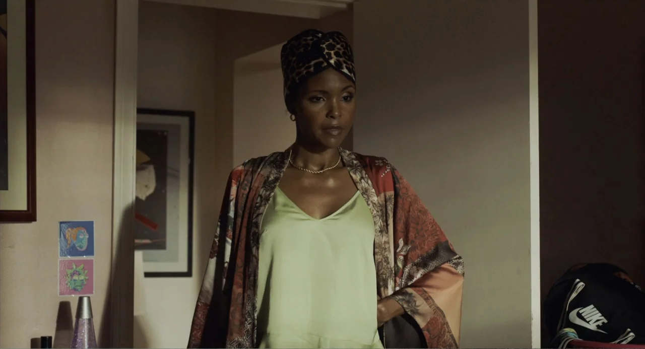 House Party (1990) movie still: medium — A woman stands in the doorway of a dimly lit room with walls. She wears a silk camisole and robe while…