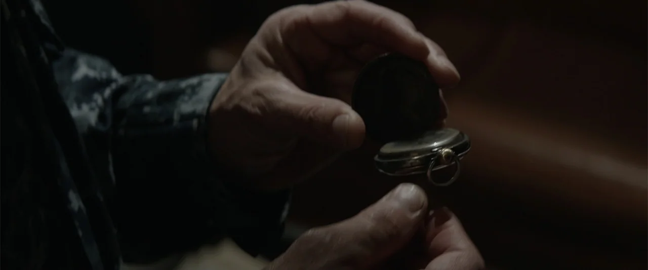 Godzilla (2014) movie still: closeup — A dark indoor space contains a pair of hands holding a metallic object. The hands display a pocket watch…