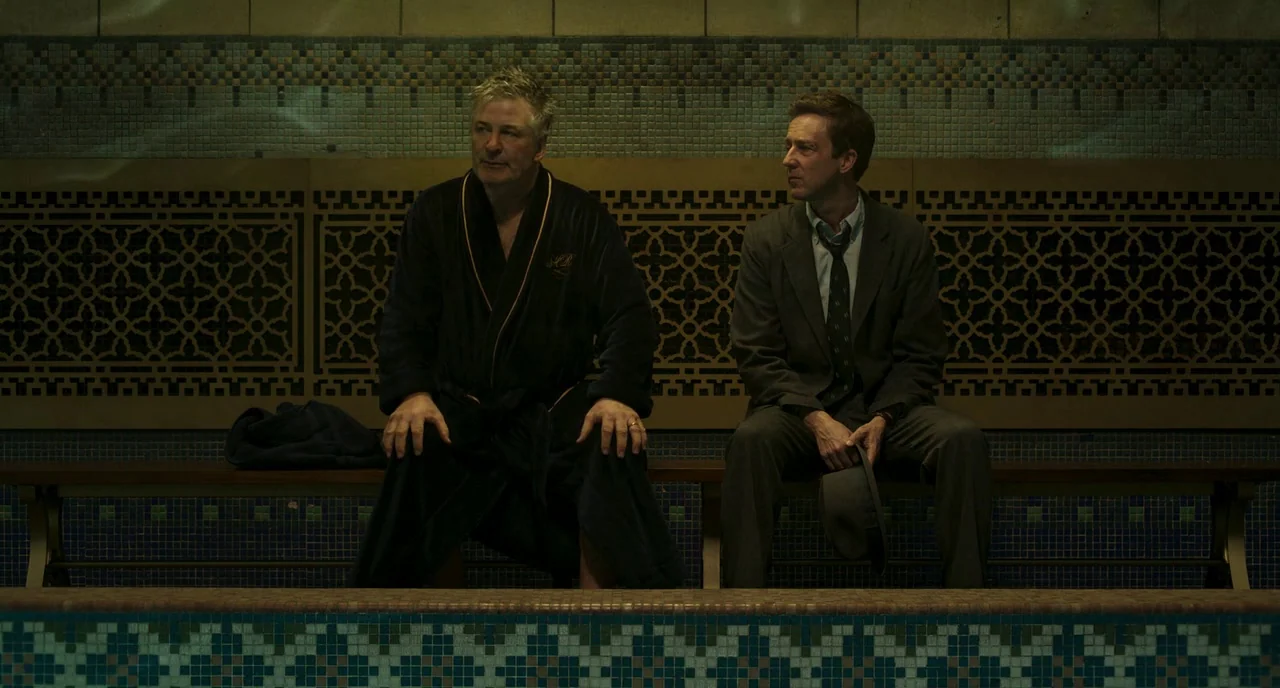Motherless Brooklyn (2019) movie still: medium — A tiled locker room features intricate mosaic patterns along the wall behind a bench. Two men in…